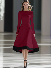 A woman wears a long-sleeved burgundy midi dress with a black hem and a cinched waist.