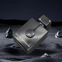 A black rectangular bottle of Armaf Club de Nuit Intense Man perfume sits on dark sand.