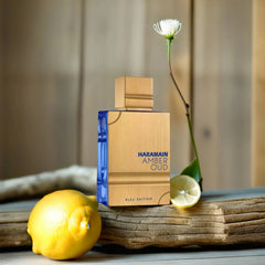 A bottle of Al Haramain Amber Oud Bleu Edition perfume sits on a wooden surface with lemons.