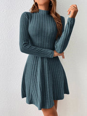 A woman wears a teal long-sleeve mini dress with a mock neck and a flared A-line skirt.