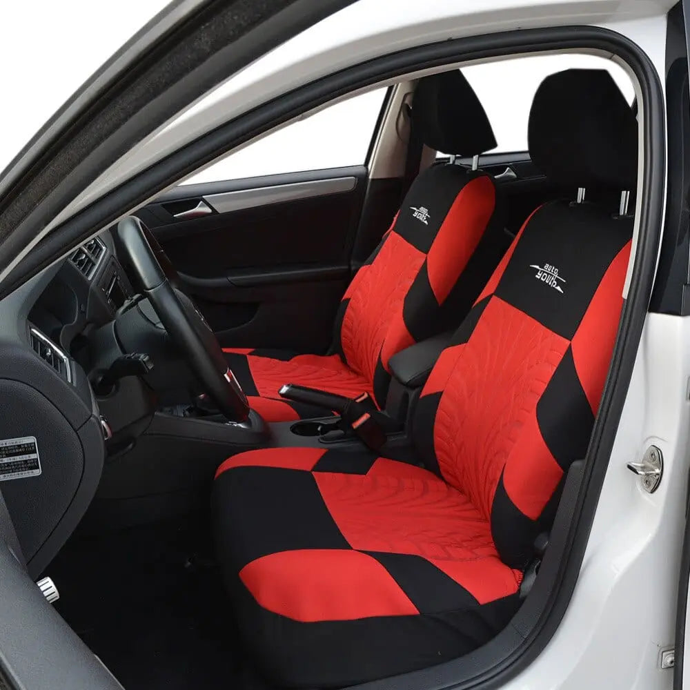 A white car’s interior shows front seats with AUTOYOUTH Fashion Tire Track Detail Style Universal Car Seat Covers in black and red polyester featuring a patterned design and printed text on the upper backrest; dashboard and steering wheel are visible.