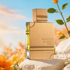 A rectangular gold bottle of Al Haramain Amber Oud Gold Edition perfume sits on a stone surface.