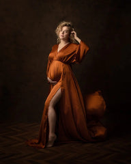 A pregnant woman wears a long, rust-colored V-neck maternity dress with a side slit.