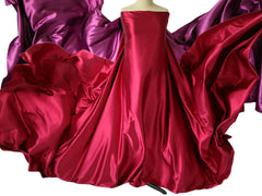 A mannequin displays a flowing, strapless red satin gown with long, dramatic fabric overlays.