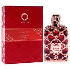 A bottle of Orientica Amber Rouge perfume next to its matching red decorative box.
