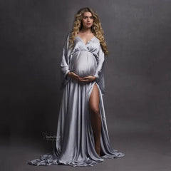 A pregnant woman wears a long, silver V-neck maternity dress with a side slit and long train.