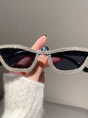 A hand holds cat-eye sunglasses with black lenses and a frame encrusted with sparkling rhinestones.