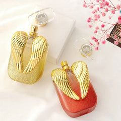 Two rectangular perfume bottles with gold angel wings, one gold and one red, on a white surface.