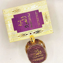 A bottle of Sheikh Al Oud perfume sits in front of its matching gold and purple decorative box.