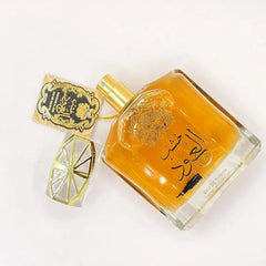 A square glass Arabian Sandalwood perfume bottle with golden liquid, ornate Arabic script, a gold-trimmed faceted cap, and tag; exclusively for Dubai UAE royal men’s and women’s fragrance, certified cosmetics quality control.