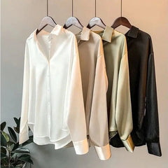Four long-sleeved, solid-colored silk-style button-down shirts hang in a row.