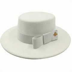 A white flat-top fedora hat featuring a matching ribbon bow and a small gold bee emblem.