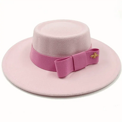 A light pink felt fedora hat with a flat top and a matching pink ribbon bow featuring a gold bee pin.