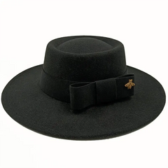 A black flat-top fedora hat featuring a matching ribbon bow and a gold bee emblem.