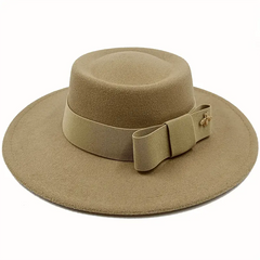 A tan flat-top fedora hat featuring a matching ribbon band with a bow and a small gold bee emblem.