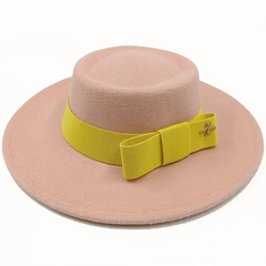 A light pink flat-top fedora hat featuring a yellow ribbon band with a bow and a small bee pin.