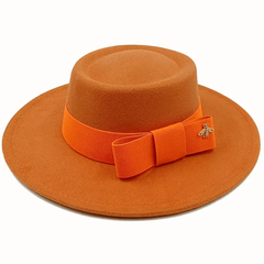 A solid orange flat-top fedora hat featuring a matching bow tie band and a small gold bee emblem.