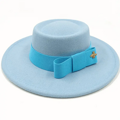 A light blue felt fedora hat with a flat top, a bright blue ribbon bow, and a small gold bee pin.
