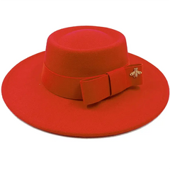 A red flat-top fedora hat featuring a matching ribbon bow and a small gold bee emblem.