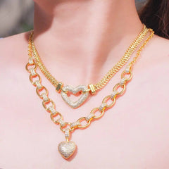 A woman wears the CWWZircons 585 Gold Color Love Heart Charm Jewelry Set: layered necklaces with cubic zirconia heart pendants, both resting stylishly on bare skin.