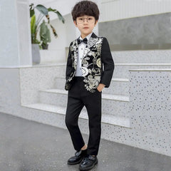 A young boy with glasses stands confidently on indoor steps, wearing the Children Formal Dress Kids Flower Jacket Pants Bowtie 3PCS—a handsome photography suit featuring a black outfit and a gold bronzing flower jacket, with his hands in his pockets.
