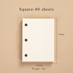 A small, square-grid loose-leaf notebook with three binder holes, measuring 61mm by 79mm.