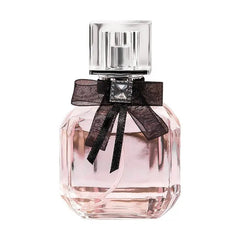 A clear glass perfume bottle filled with pink liquid, featuring a black bow and a square cap.