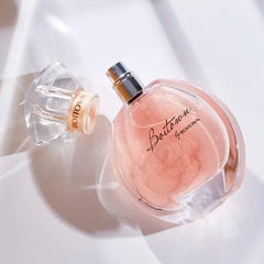A round glass perfume bottle filled with shimmering pink liquid and a detached matching cap.