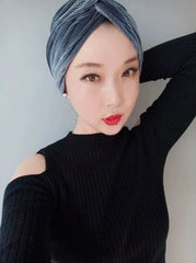A woman wears a gray velvet turban-style cap with a pleated, dome-shaped design.