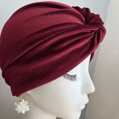 A deep red ribbed velvet turban hat worn on a mannequin head.