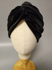 A black velvet turban-style cap with a pleated design displayed on a mannequin head.