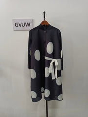 An Elegant Stand Collar Pleated Dress in black with large white polka dots, a white waist bow, and knee-length cut is displayed on a hanger. A sign reading GVUW is mounted on the wall behind it.