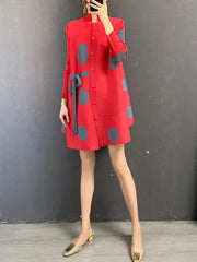 A person stands against a gray wall wearing the Elegant Stand Collar Pleated Dress, which is red with large gray polka dots, a matching belt, and knee-length long sleeves. Beige low-heeled shoes complete the look. The person's face is not visible.