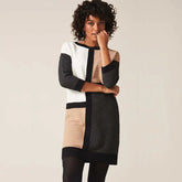 A woman wears a long-sleeved, color-blocked knitted dress with a crew neck and ribbed texture.