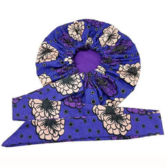 A purple satin sleep bonnet featuring a floral African print and an adjustable wide tie band.