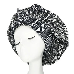 A black and white patterned satin sleep bonnet with an adjustable wide band on a mannequin head.