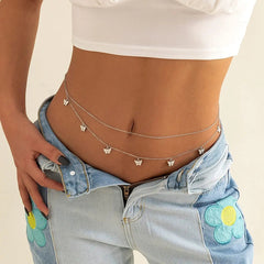 A person wears light blue jeans with flower patches, a white crop top, and the Fashion Classic Cute Butterfly Waist Chain—a simple, sexy body jewelry piece—draped around their waist above slightly lowered boho jeans.