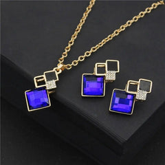 A gold-tone jewelry set featuring a necklace and earrings with geometric blue crystal pendants.