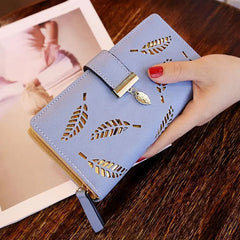 A light blue long wallet with gold hollow leaf cutouts and a matching leaf charm.