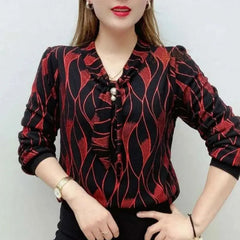 A woman wears a long-sleeved black V-neck blouse with a red wave pattern and pearl embellishments.