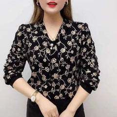 A woman wears a black long-sleeved V-neck blouse featuring a gold floral print and pearl accents.