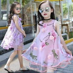 Two girls in matching "Girls Flower Dress Kids Girl Beach Dresses Chiffon" stand outdoors, both wearing sunglasses. One faces forward with a choker, while the other faces sideways. Both dresses feature a floral print.
