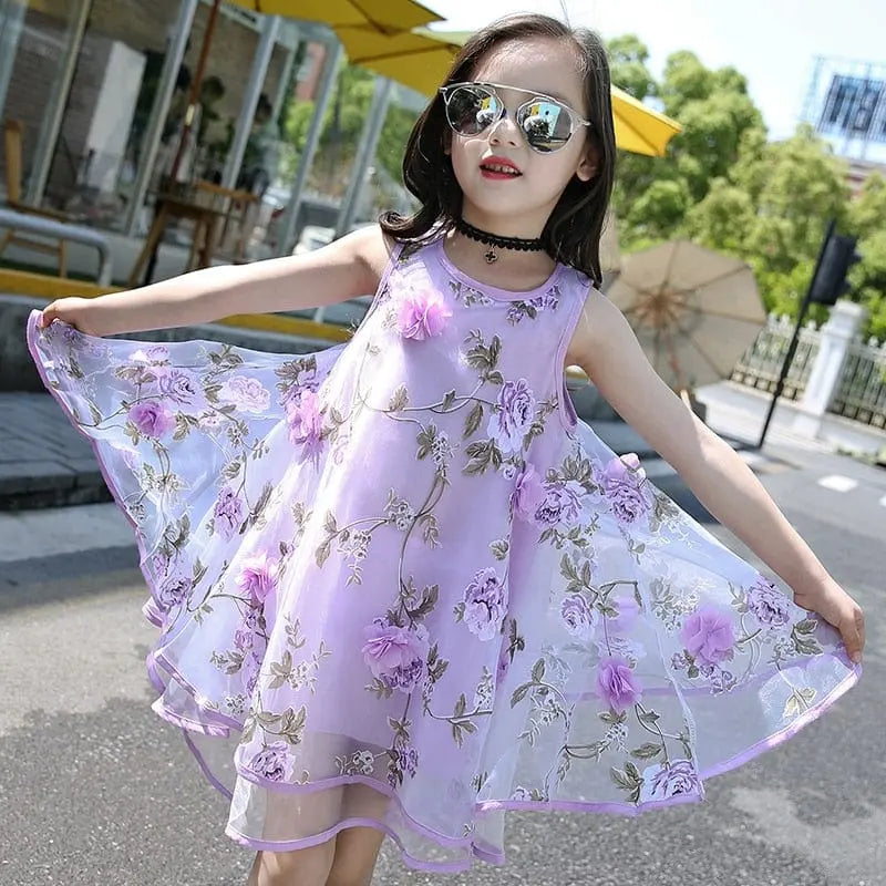 A girl twirls outdoors on a sunny day, wearing the Girls Flower Dress—chiffon floral beach dress for kids ages 6–14—surrounded by large parasols and lush greenery.