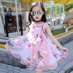 A young girl in reflective sunglasses poses outdoors in a Girls Flower Dress Kids Girl Beach Dresses Chiffon, standing on a stone path with yellow umbrellas and greenery in the background.