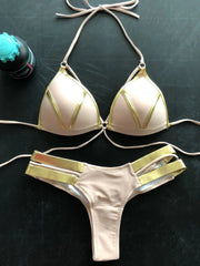 A beige bikini set featuring gold metallic trim on the triangle top and double-strap bottoms.