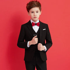A young boy wears a formal black suit with a white shirt and a red bow tie.