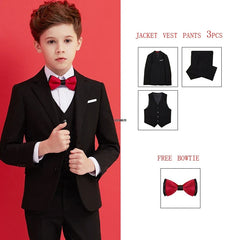 A boy wears a black formal suit set consisting of a blazer, vest, pants, and a red bowtie.