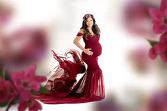 A pregnant woman wears a floor-length, off-the-shoulder red chiffon maternity dress.