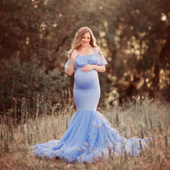 A pregnant woman wears a light blue off-shoulder mermaid maternity gown with ruffled details.