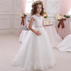 A girl wears a white floor-length ball gown with lace appliques and a beaded waist sash.